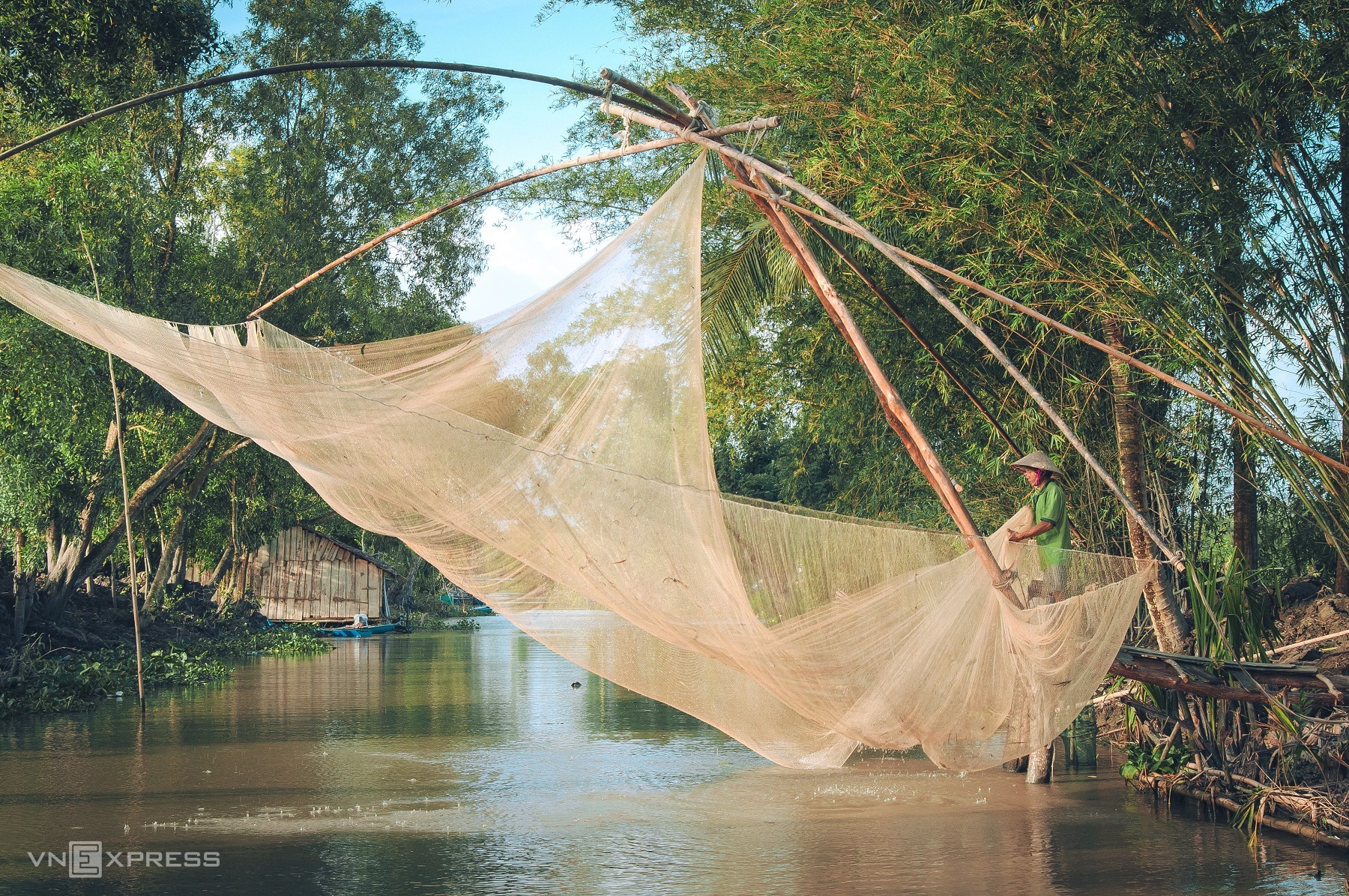 Рыбак использует большую сеть, натянутую на старые бамбуковые планки, для ловли рыбы и креветок в сезон наводнений.