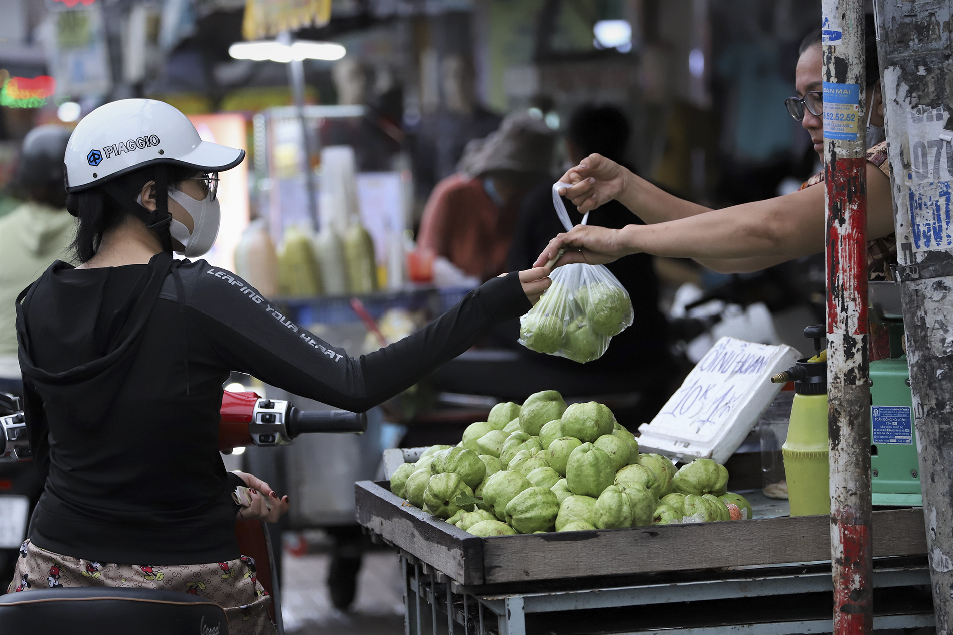 Продавец фруктов передает гуаву, завернутую в полиэтиленовый пакет, клиенту на местном рынке.