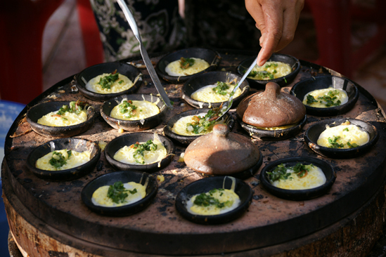 Бань кан, вьетнамские маленькие рисовые блины, готовятся на маленькой глиняной сковороде на светящемся угле в ларьке в Камране. Фото: Mr.True