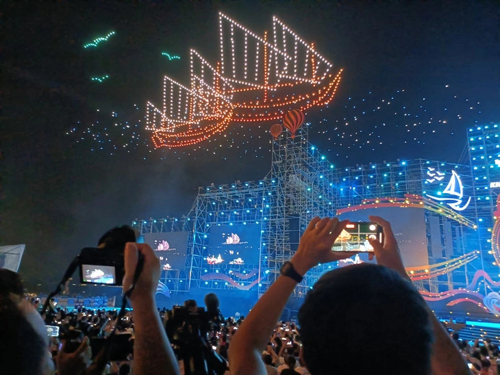 Посетители фотографируют на свои смартфоны одно из световых представлений дронов на церемонии открытия пляжного фестиваля Нячанг – Кханьхоа 2023 в городе Нячанг, 3 июня 2023 года. Фото: Tuoi Tre